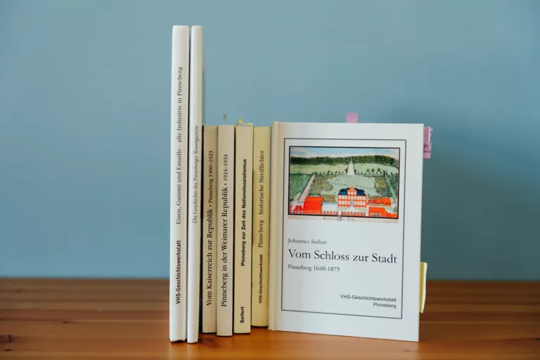 Diverse Bücher stehen auf einem Holztisch vor einer blauen Wand, die Publikationen stammen von der VHS Geschichtswerkstatt Pinneberg